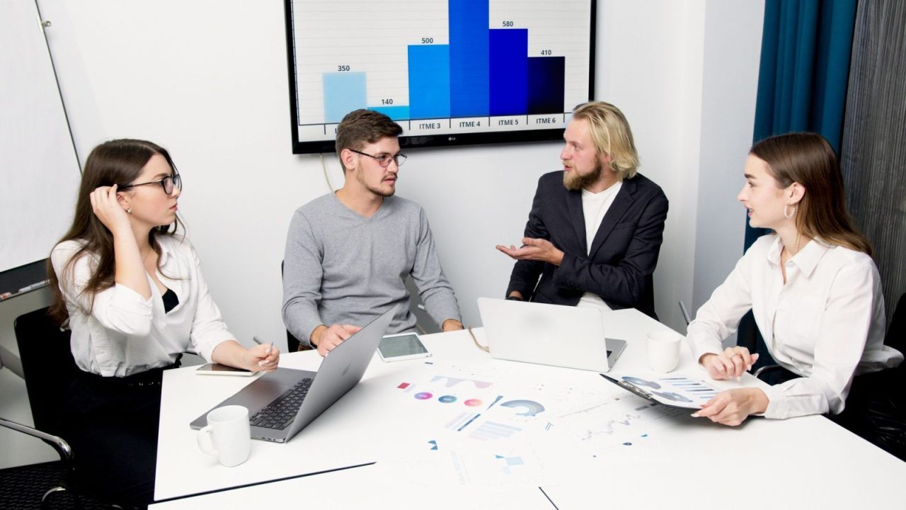 Des professionnels discutent de données autour d'une table avec ordinateurs portables et graphiques