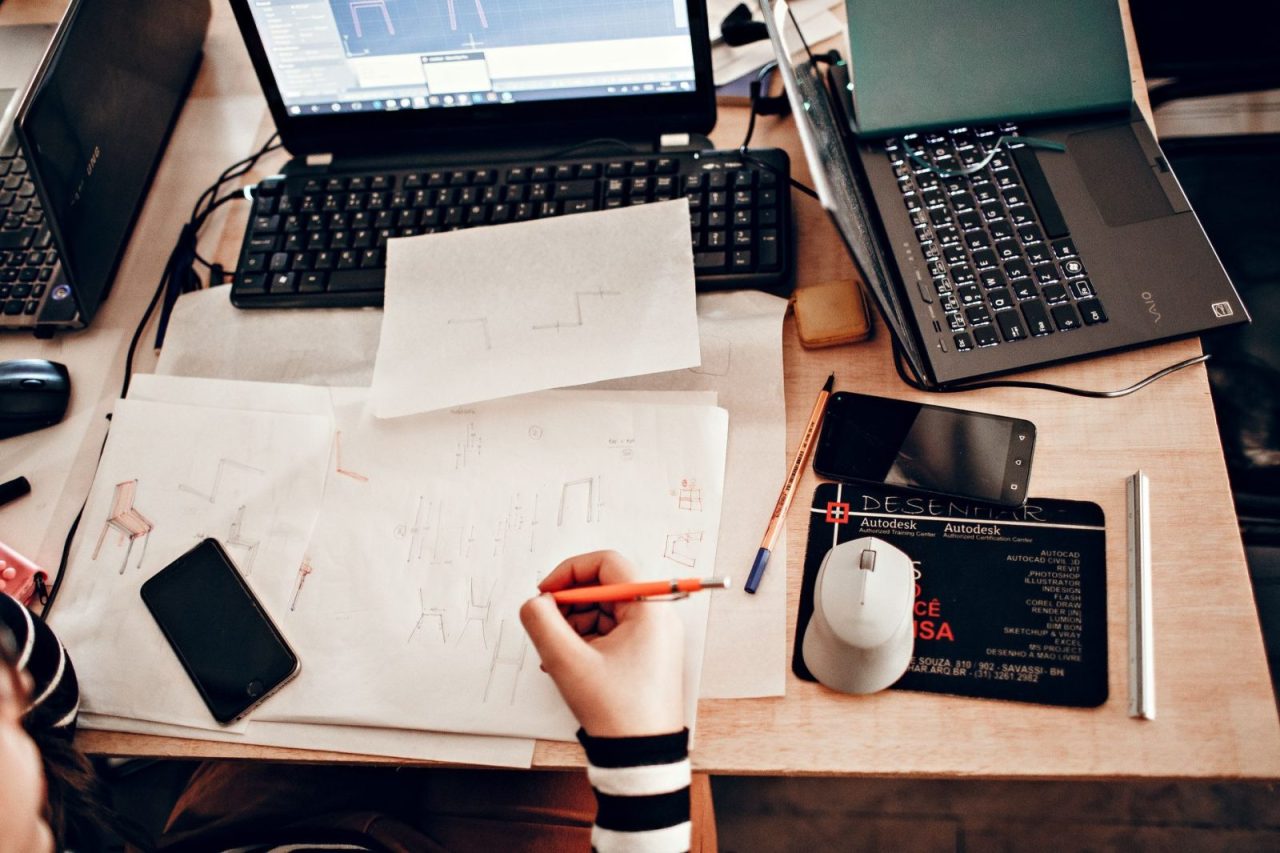 Workspace with sketches, laptops, and drawing tools viewed from above