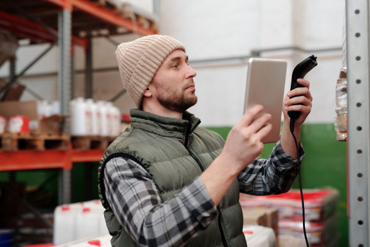 Man in a beanie and vest scanning inventory in a warehouse