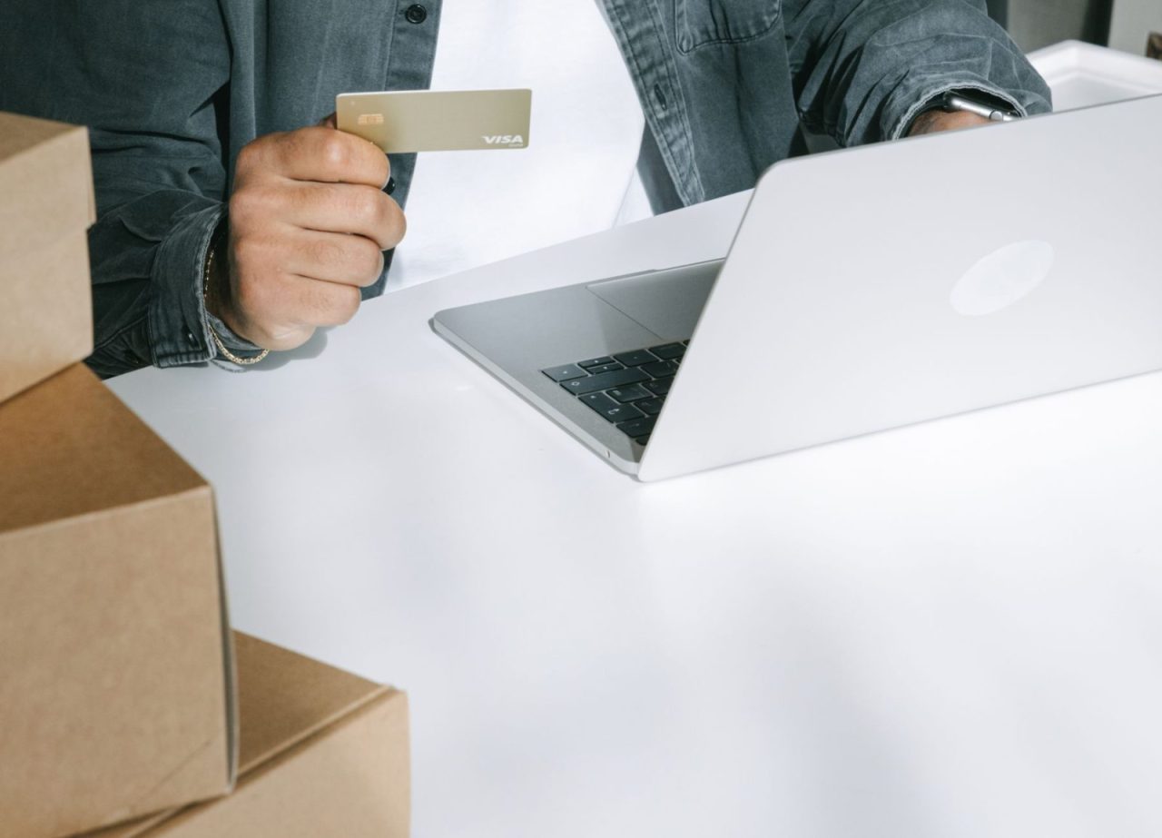 Person holding a credit card shopping online on a laptop with shipping boxes nearby