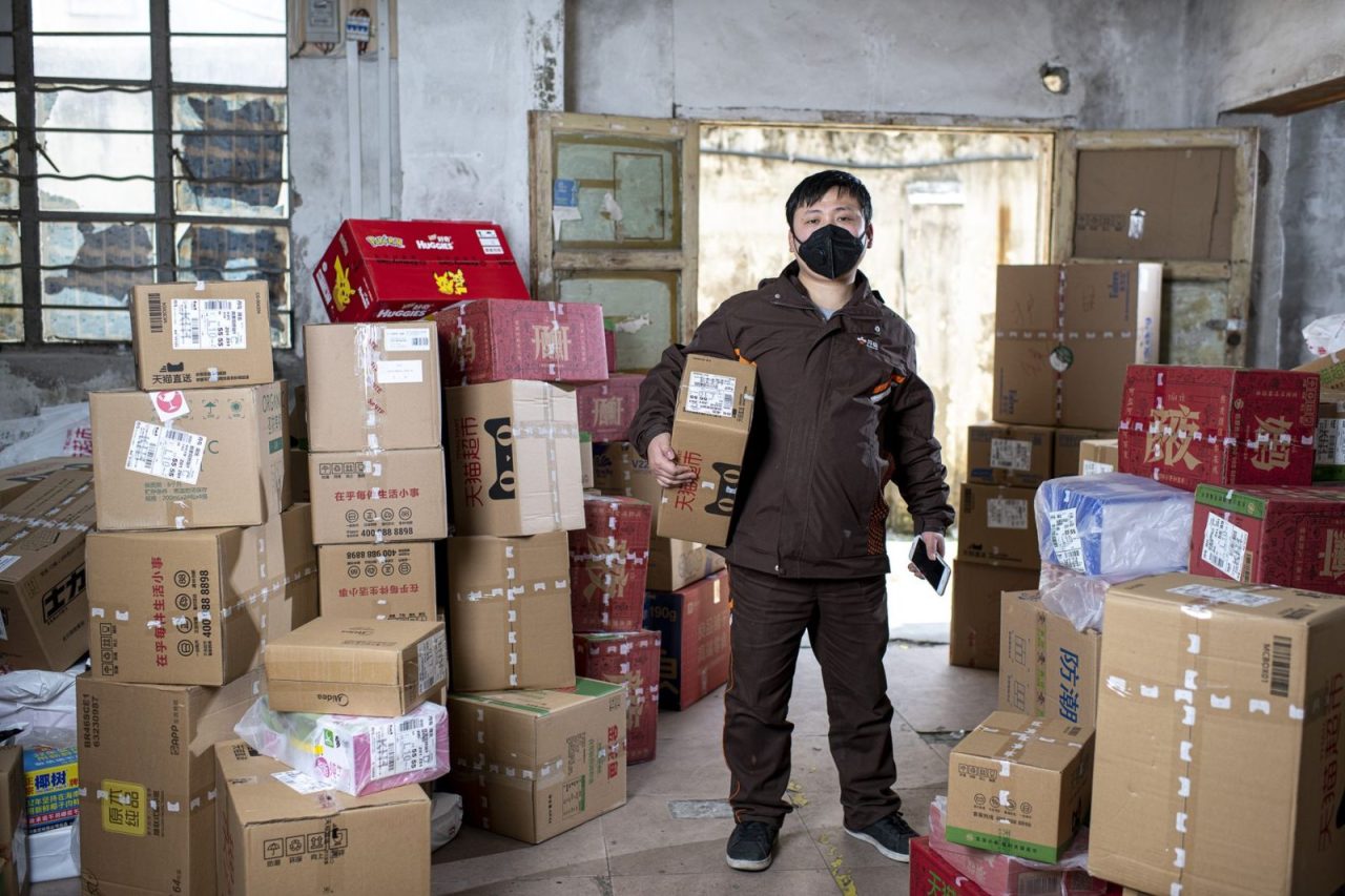 Delivery worker in a Wuhan warehouse holding packages and wearing a face mask
