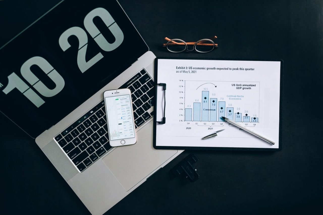 Desk setup with laptop displaying analytics dashboard, smartphone, and printed graphs