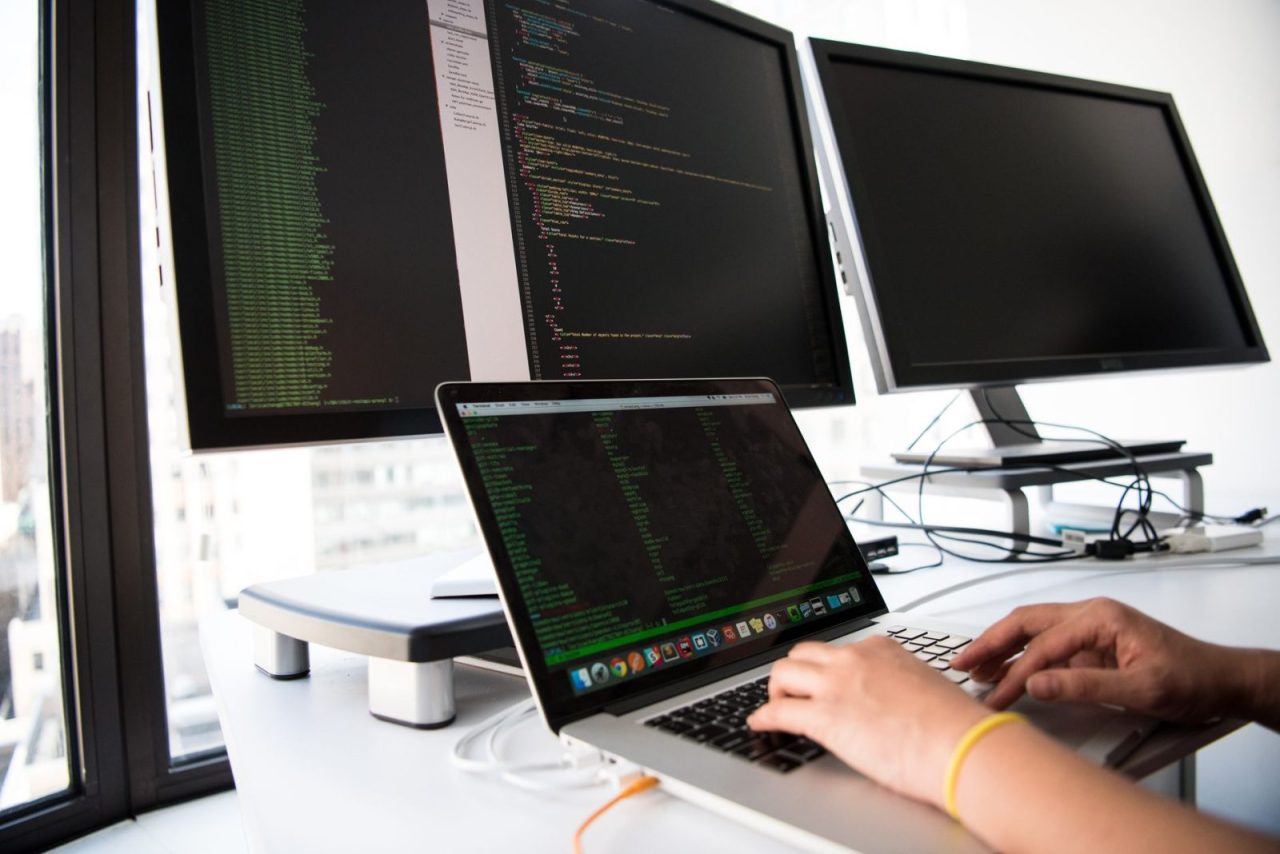 Developer writing code on a laptop with multiple monitors in an office