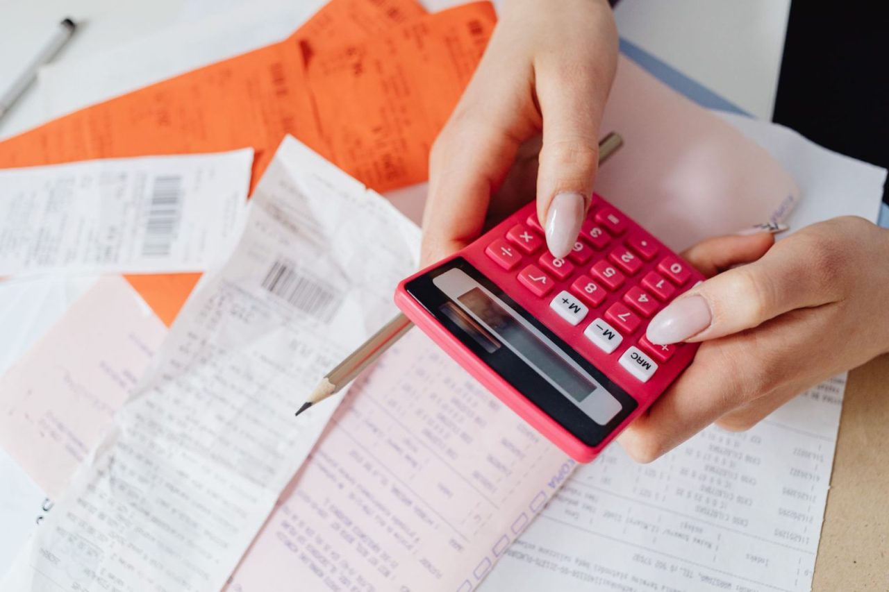 Hands using a pink calculator with receipts and documents spread out
