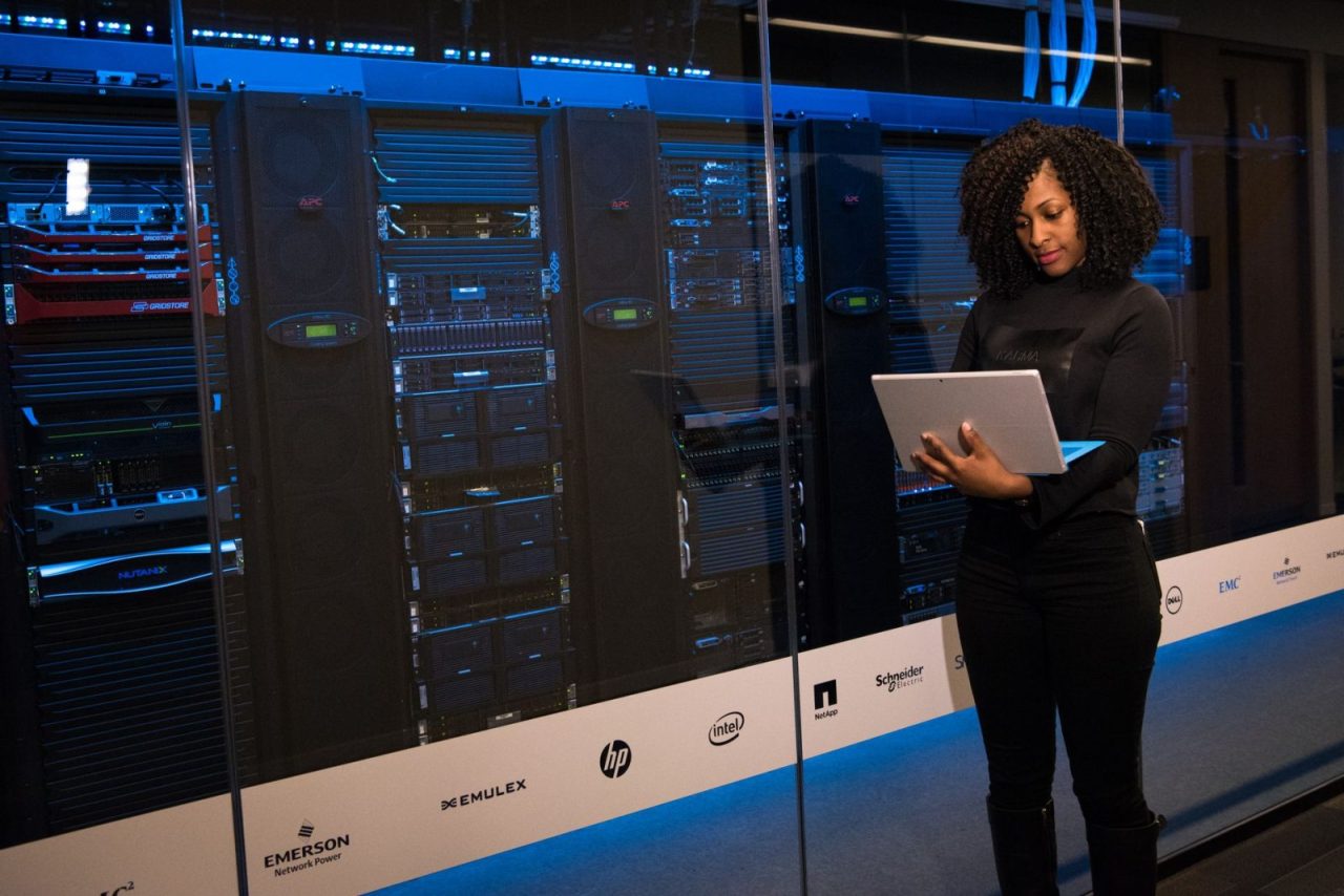 Female engineer using a laptop while monitoring data servers in a server room