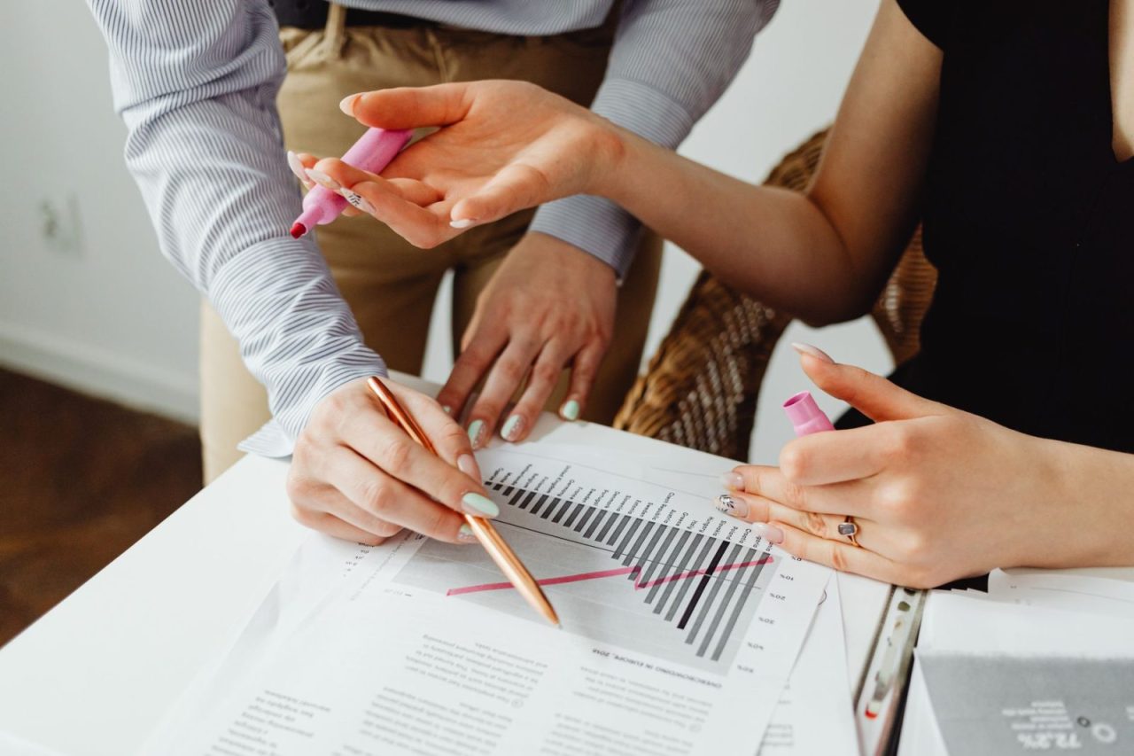 Two people collaborating on business chart analysis with markers in an office