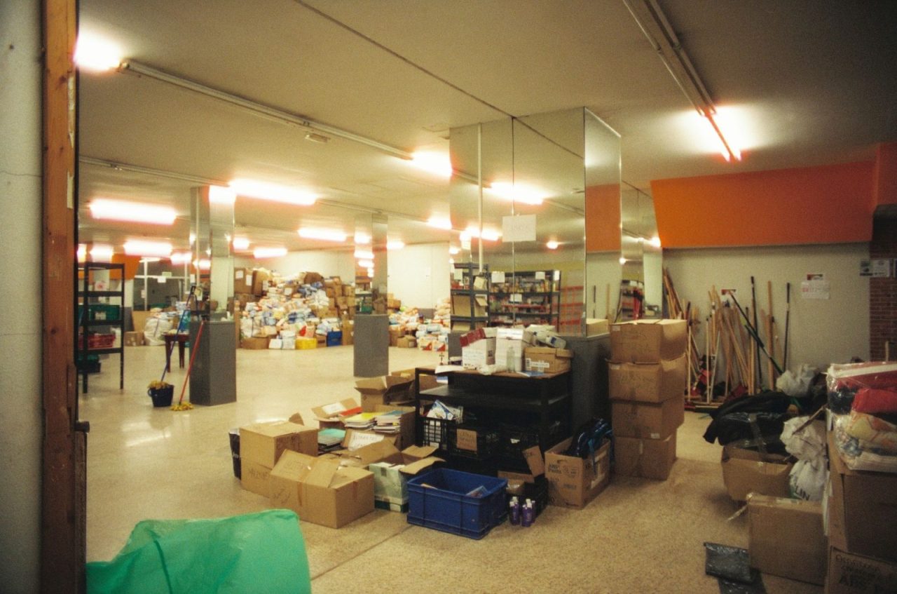 Large indoor storage area with stacks of boxes and supplies under fluorescent lights