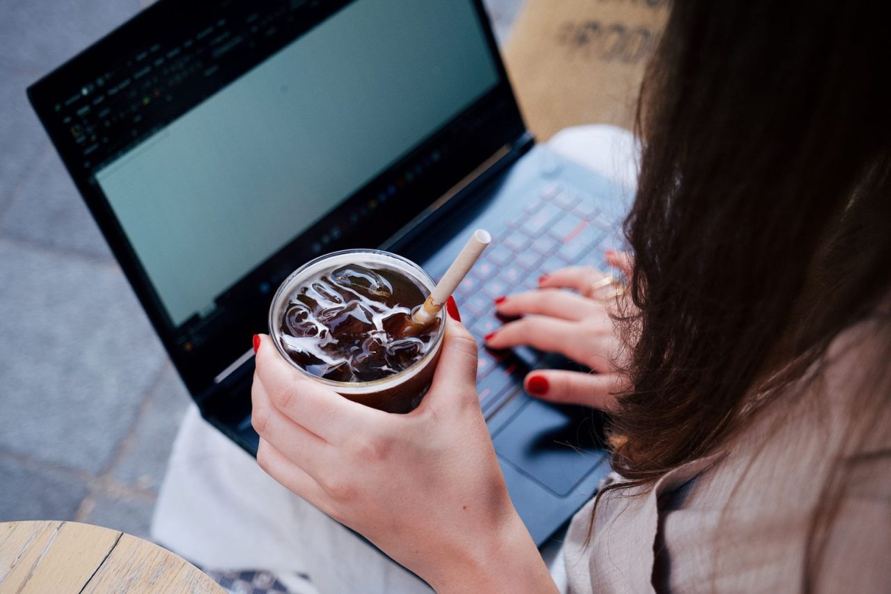 Femme adulte travaillant sur un ordinateur portable en terrasse avec une boisson glacée