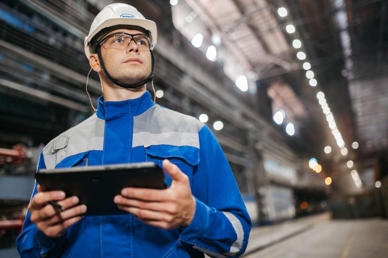 Factory worker in safety gear using a tablet in an industrial environment