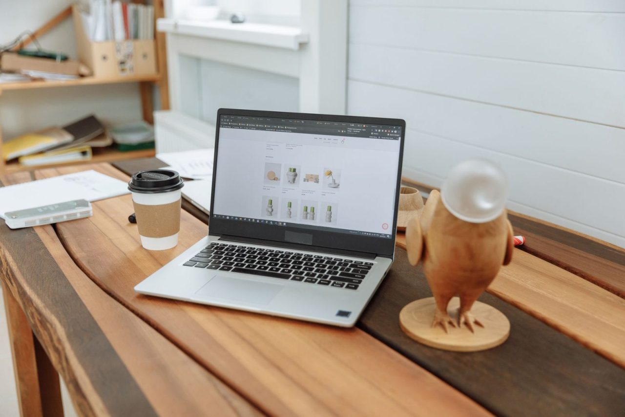 Laptop, coffee cup, and wooden figurine on a wooden office desk