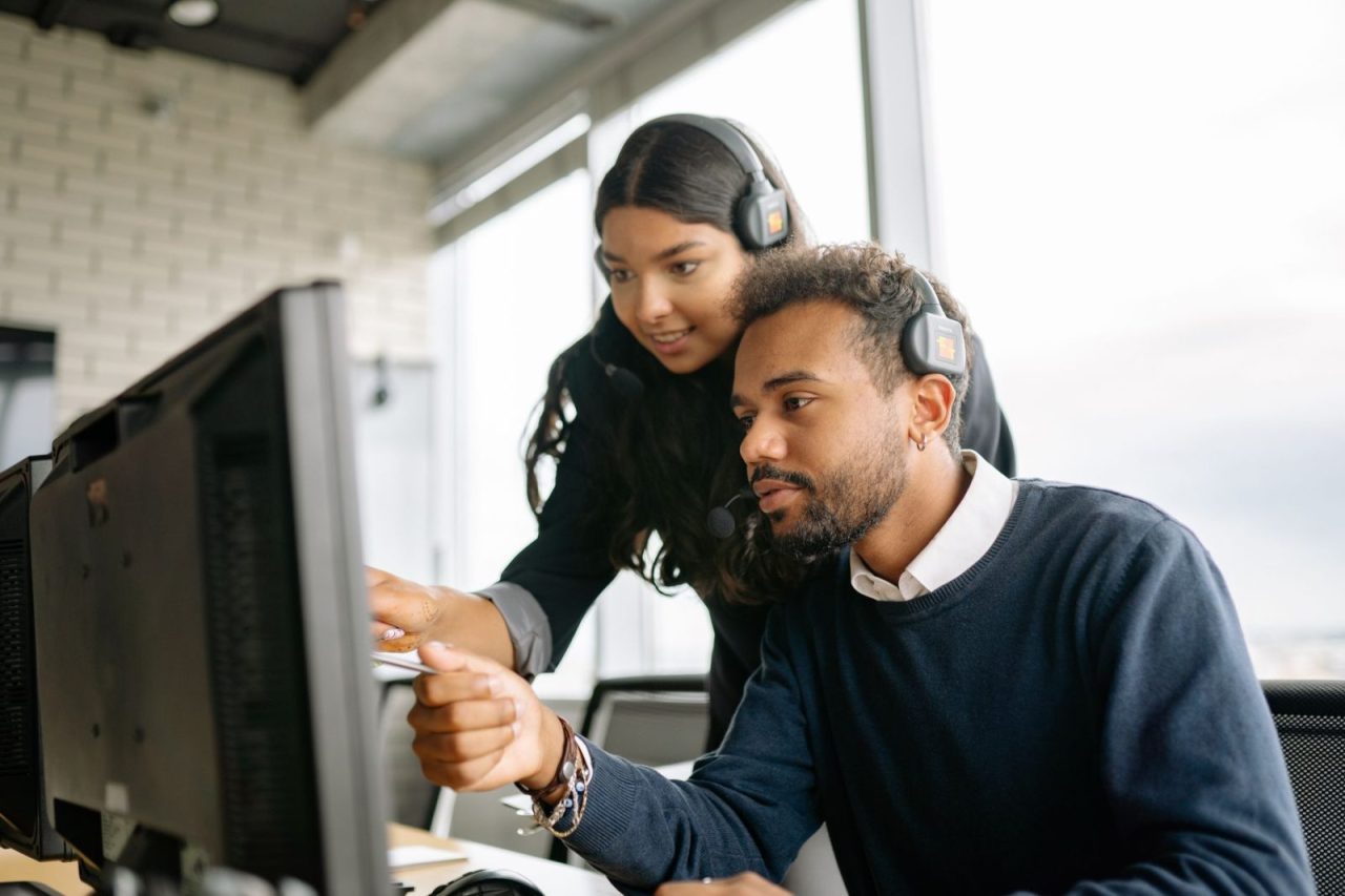 Two call center employees wearing headsets working together in a modern office