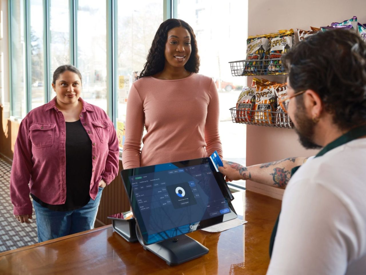 Two women completing a payment at a convenience store using a touchscreen POS system