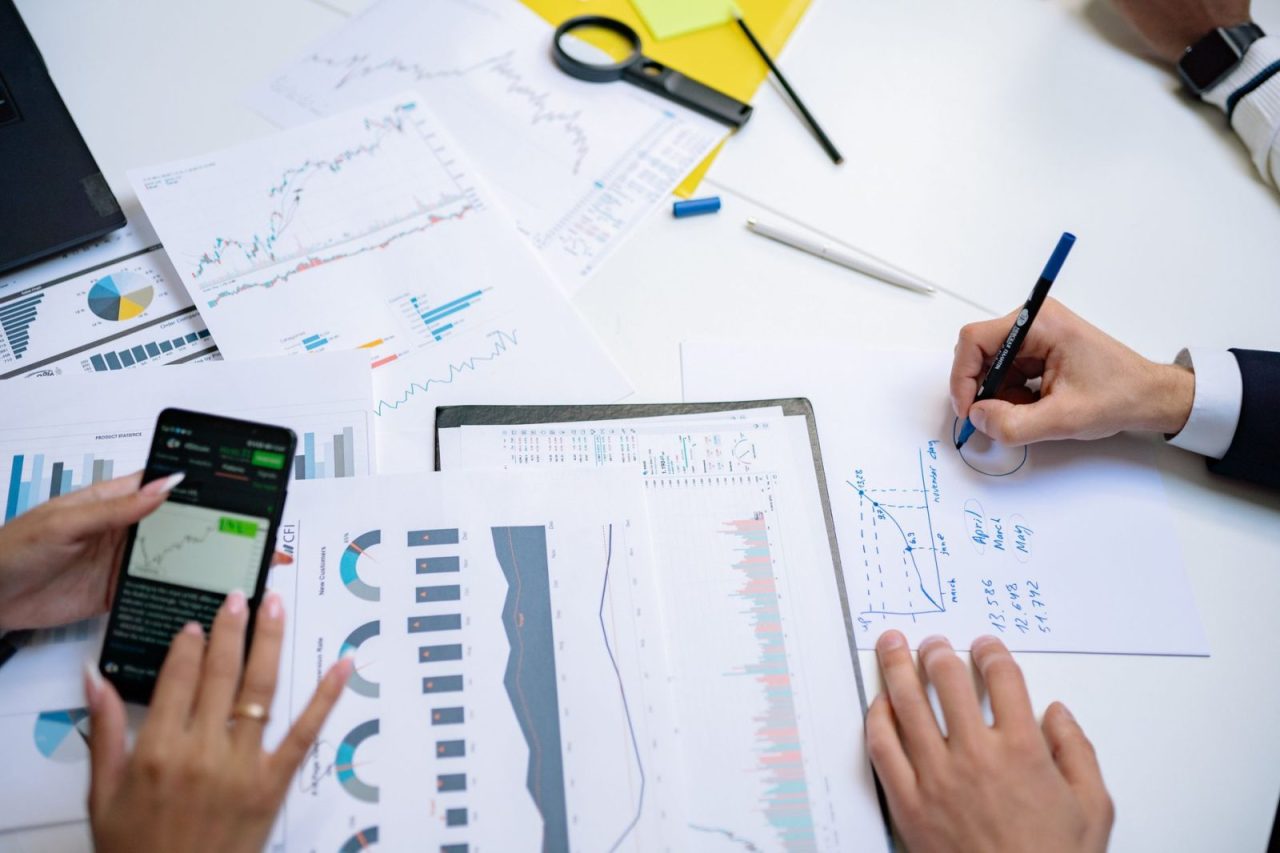 Collègues analysant des graphiques financiers sur mobile et documents papier au bureau
