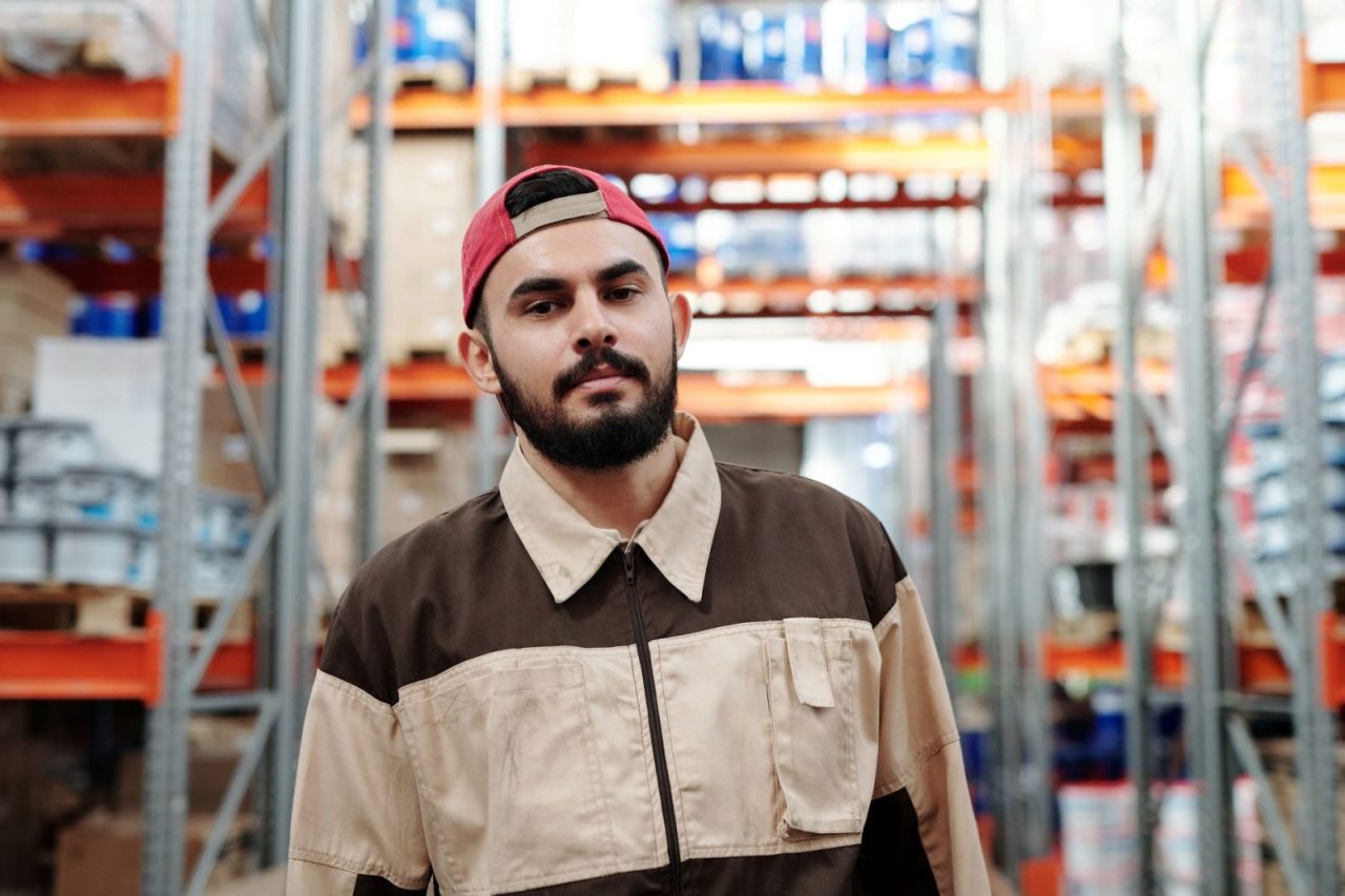 Warehouse worker in uniform standing among shelves and packages