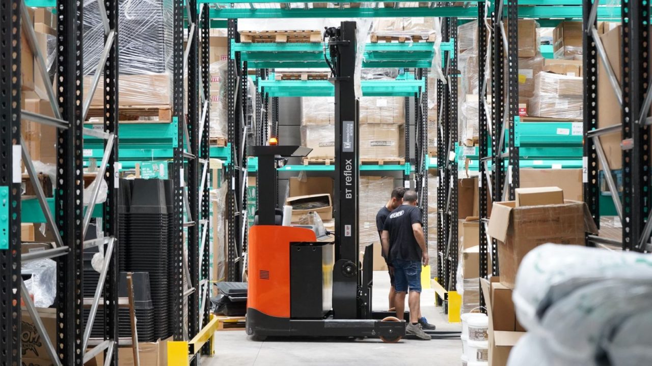 Workers and a forklift moving through warehouse aisles for logistics and inventory tasks