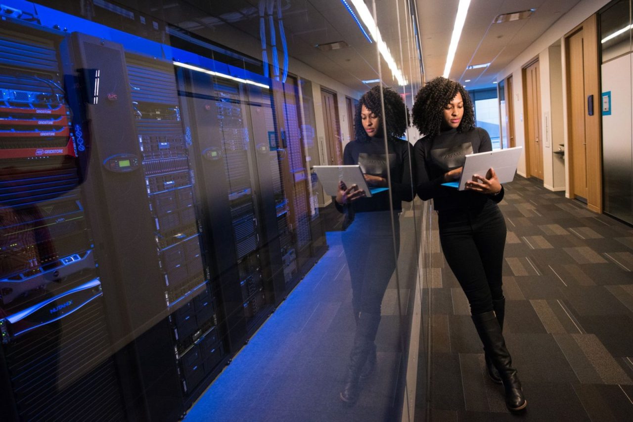 Woman with a laptop navigating a data center aisle lined with mirrored servers