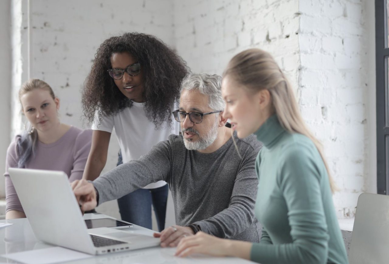 Man at a table explaining project details on a laptop to two women