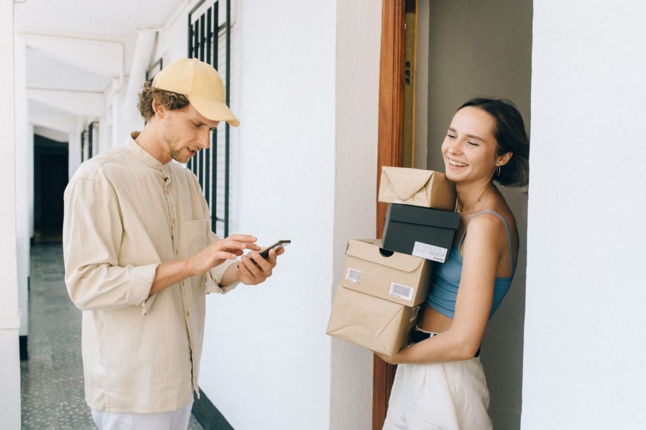 Woman receives a delivery in a hallway and uses her smartphone for online payment