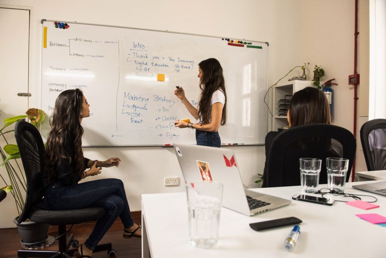 Business women discussing strategy at a whiteboard in a modern office