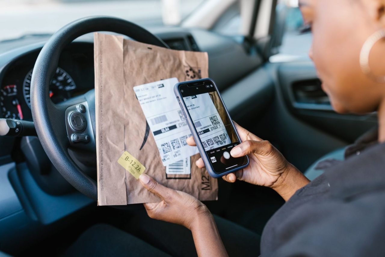 Courier in a car scanning a package label with a smartphone